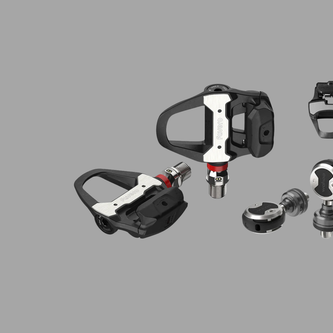 Road cyclist climbing with power meter pedals syncing metrics to head unit for training analysis