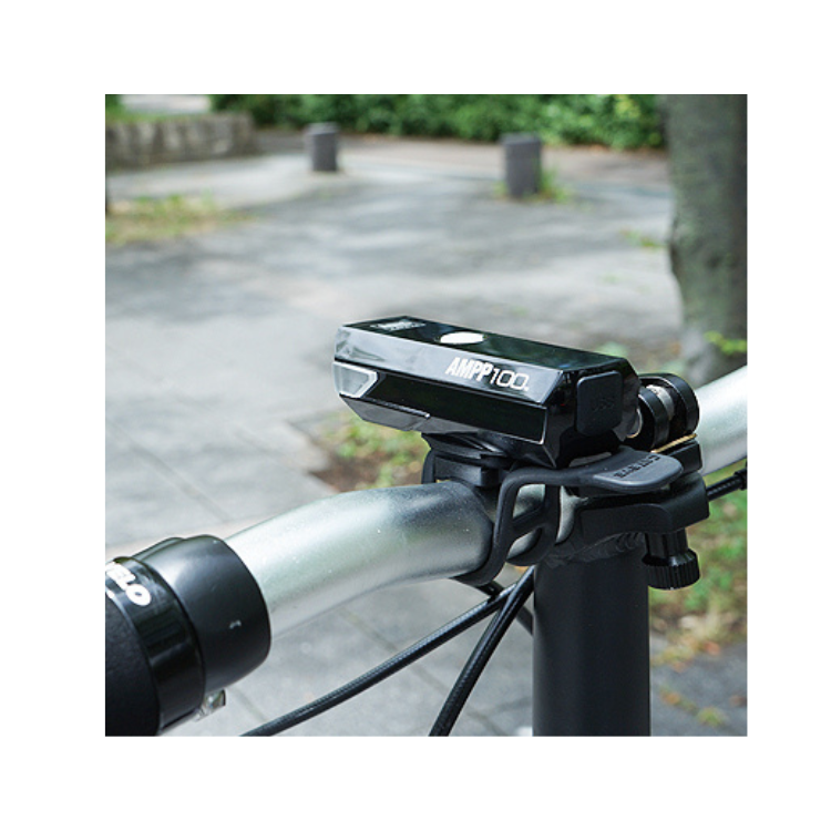 Close-up of the Cateye AMPP100 front bike light mounted on the handlebar of a bicycle, showing the light in its active position for clear illumination.