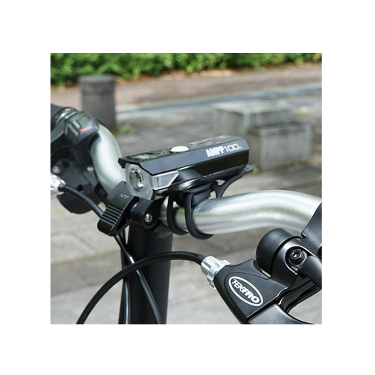 Cateye AMPP 100 bike headlight mounted on a handlebar, providing clear illumination for night cycling, with a close-up view of its mounting system.