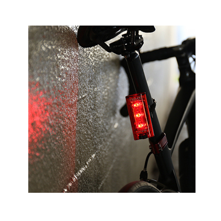 Cateye Tight Kinetic rear light mounted on a bicycle, casting a red light on the wall, demonstrating its bright visibility for cycling safety.