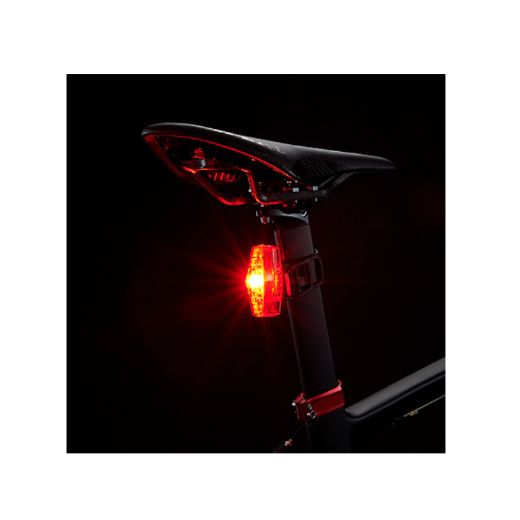 Cateye VIZ150 red rear bike light mounted on a bicycle seat post glowing brightly in a dark setting.