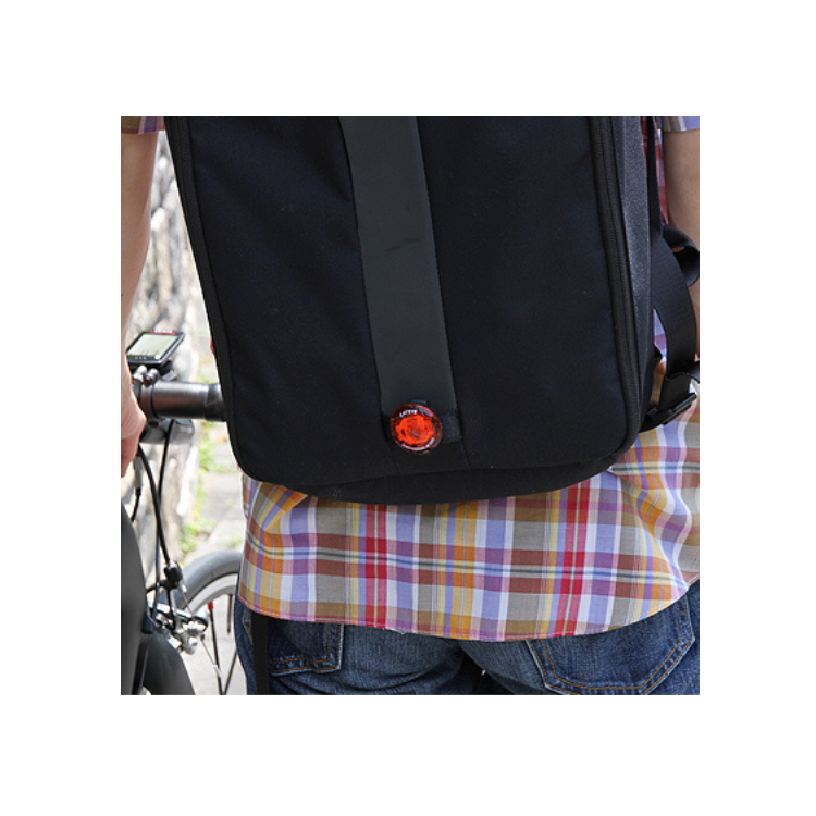 Cateye wearable mini LED light attached to the back of a backpack, enhancing visibility and safety for cyclists or pedestrians.