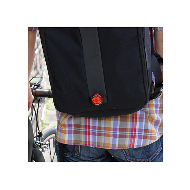 Cateye wearable mini LED light attached to the back of a backpack, enhancing visibility and safety for cyclists or pedestrians.