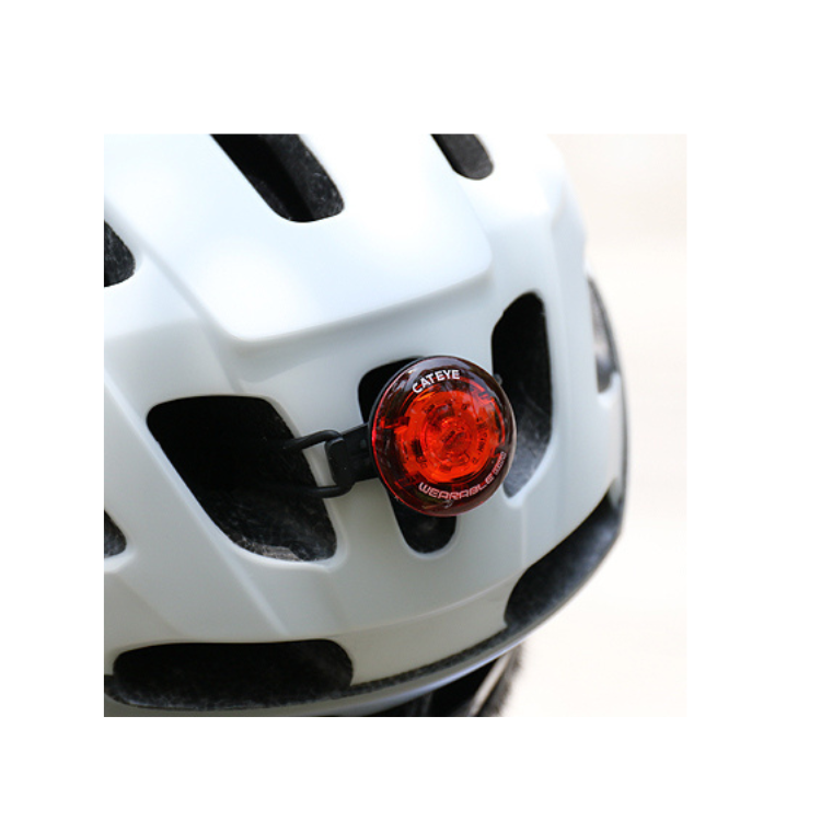 Cateye wearable LED light attached to a bicycle helmet, increasing visibility for cyclists in low-light environments.