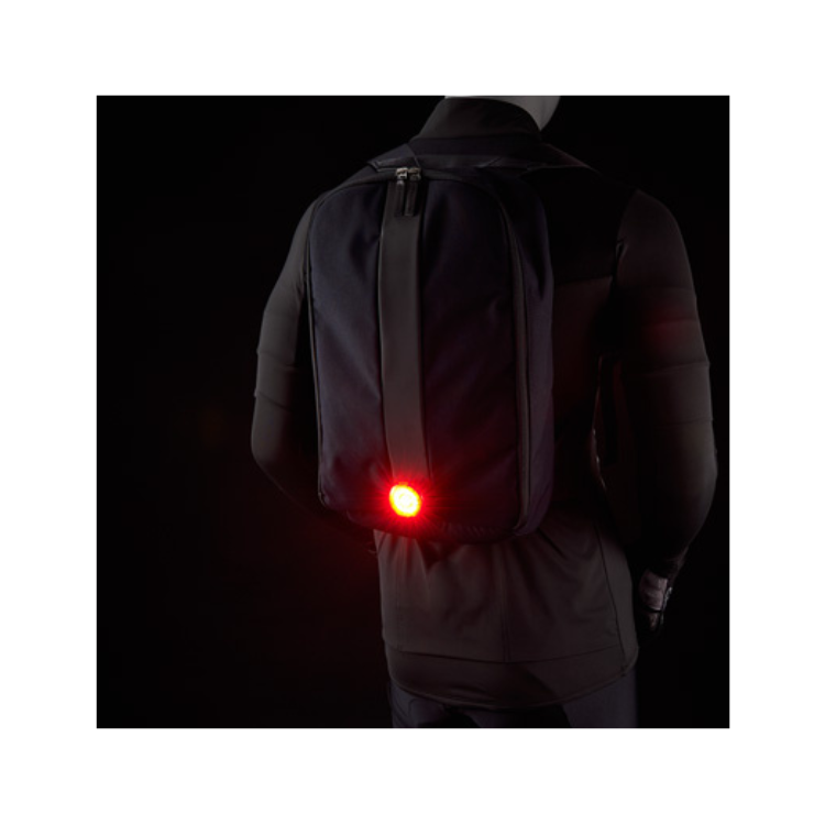 Cateye wearable LED light fixed to a backpack, offering enhanced visibility for cyclists or pedestrians in low-light settings.