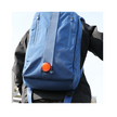Person wearing a blue backpack with a red Cateye rear safety light clipped to the back, increasing visibility while cycling or walking.