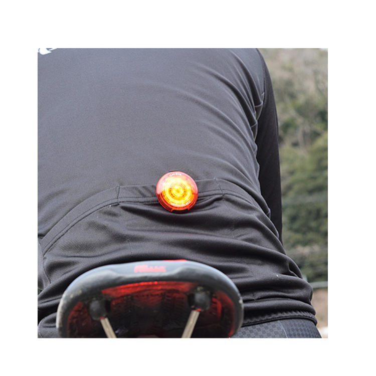 Cyclist wearing a black jersey with a red Cateye rear safety light clipped to the back pocket for enhanced visibility.