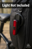 Black backpack with a red bike light attached, blurred background