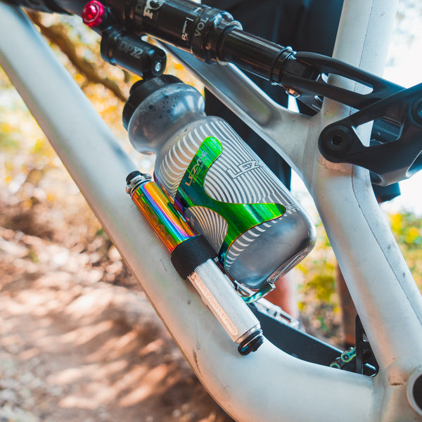 Silver and rainbow Lezyne Pocket Drive Pro mini pump mounted securely on a mountain bike frame alongside a water bottle.