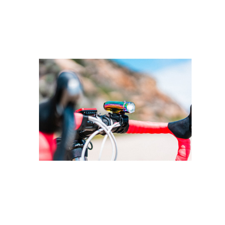 Lezyne Classic Drive 700XL front bike light in rainbow finish, mounted on the bike handlebar with red grips, providing bright visibility for cyclists.