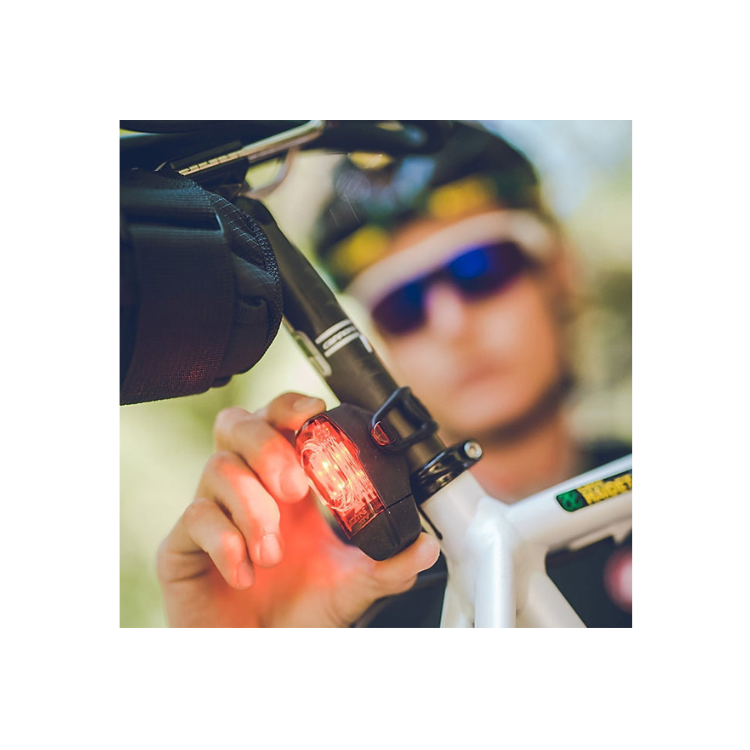 Cyclist adjusting the Lezyne KTV Pro 75 rear bike light, mounted on a white bicycle, with the red light illuminated for visibility.