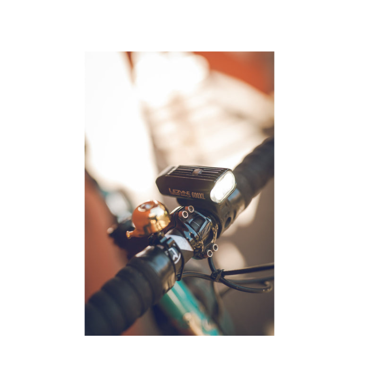 Lezyne Micro Drive 600XL front bike light mounted on the handlebar alongside a bike bell, highlighting its compact design and bright LED.