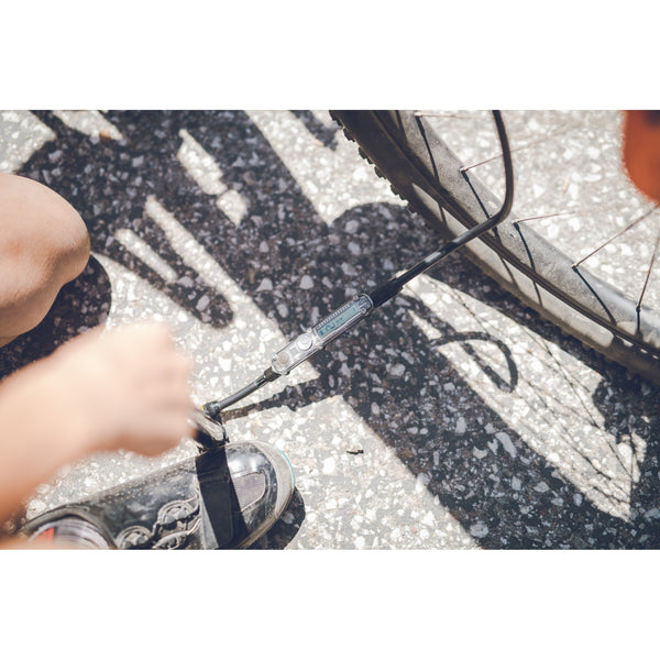 A close-up shot of a person using the Lezyne Digital Pressure Drive pump to inflate a bicycle tire on the ground.