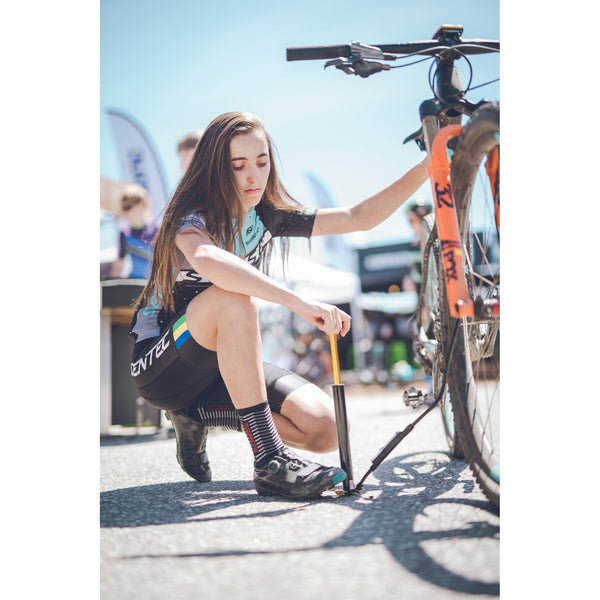 A cyclist adjusting the Lezyne Digital Pressure Drive pump while inflating a tire, on a sunny outdoor track.
