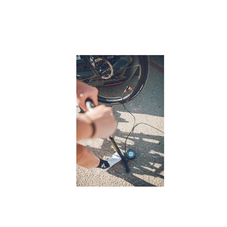 Cyclist inflating a bicycle tire with a Lezyne floor pump featuring a base gauge.