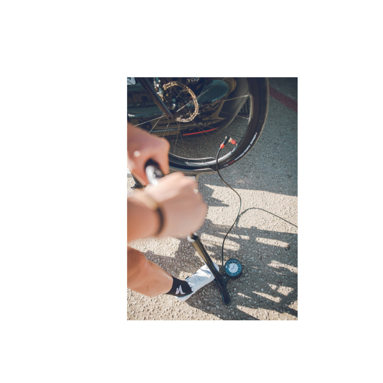 Cyclist using a Lezyne floor pump with gauge to inflate a bicycle tire outdoors.