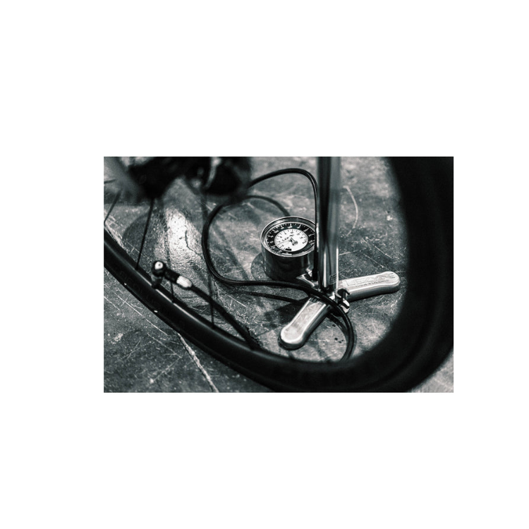 Black and white photo of a Lezyne floor pump with analog gauge and hose attached to a bicycle wheel.