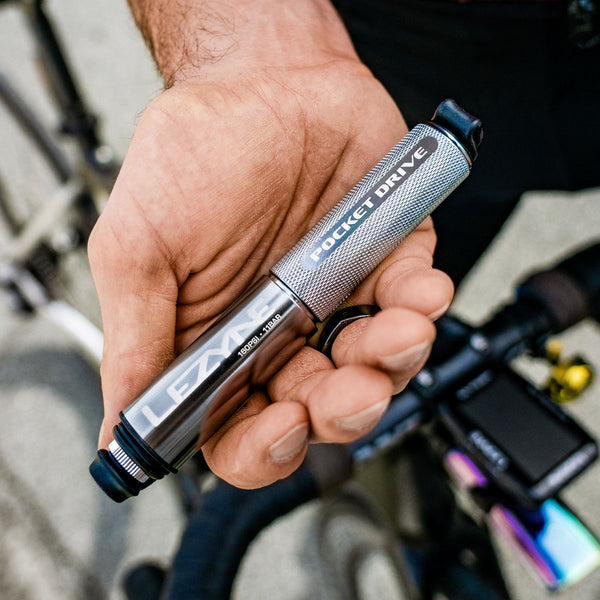 Cyclist holding a compact Lezyne Pocket Drive mini pump in metallic silver finish.