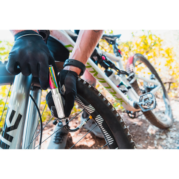 Cyclist wearing gloves using a Lezyne Pocket Drive Pro pump to inflate a mountain bike tire on a trail.