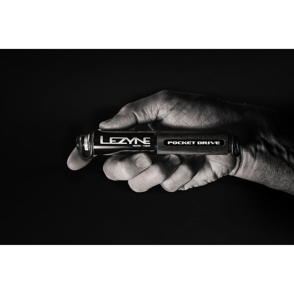 Hand holding a Lezyne Pocket Drive mini pump in a dramatic black-and-white photo against a dark background.