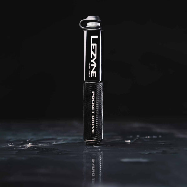 Black Lezyne Pocket Drive pump standing vertically on a wet reflective surface, showing its compact size and rugged grip.