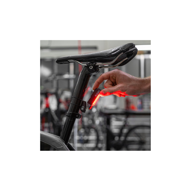 A person installing the Lezyne Stick Drive 30 bike tail light on a saddle post with the light turned on, showing its red LED glow.