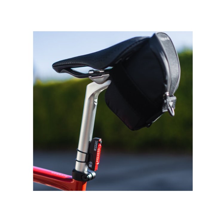 The Lezyne Stick Drive 30 bike light mounted on the seat post of a red bicycle, next to a black saddle bag.