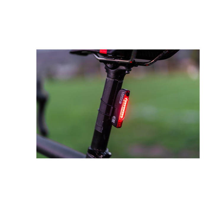 Lezyne Stick Drive 30 bike light mounted on the seat post of a bicycle, emitting a red light, with a blurred green background.